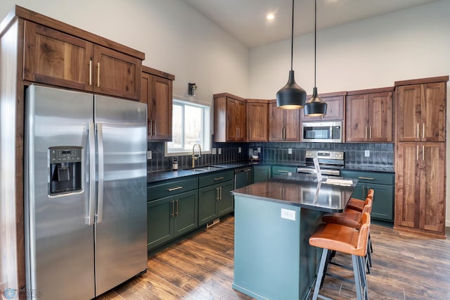 kitchen with hanging light fixtures, dark hardwood / wood-style flooring, appliances with stainless steel finishes, a kitchen island, and a kitchen bar