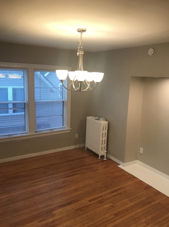 unfurnished dining area featuring radiator, dark wood-type flooring, an inviting chandelier, and plenty of natural light