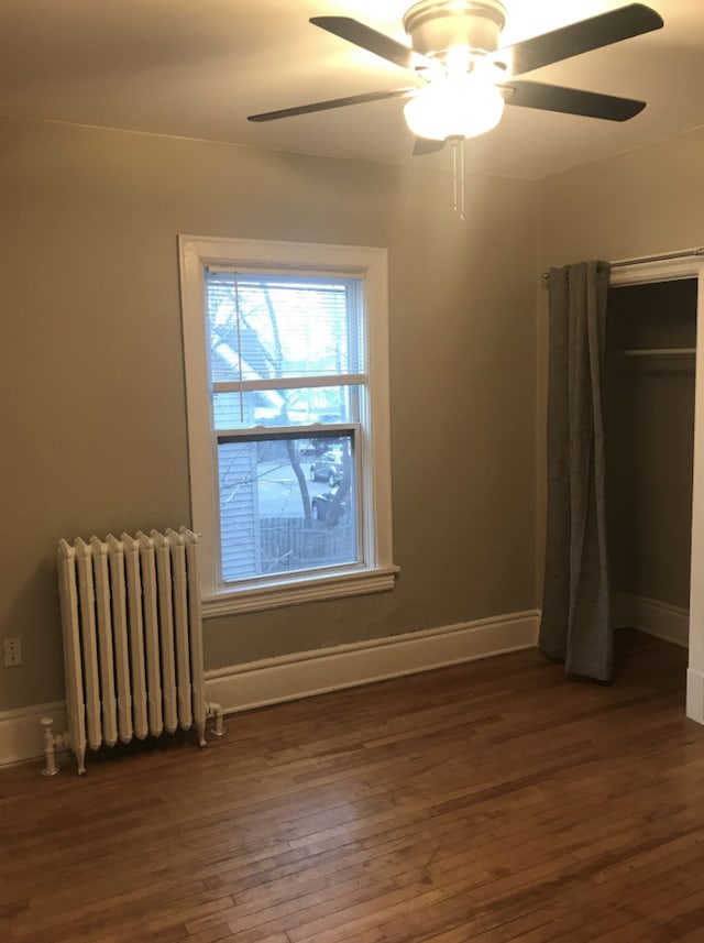 unfurnished bedroom featuring radiator heating unit, ceiling fan, and dark hardwood / wood-style floors