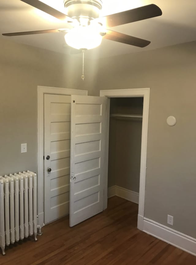 unfurnished bedroom featuring a closet, ceiling fan, radiator heating unit, and dark hardwood / wood-style flooring