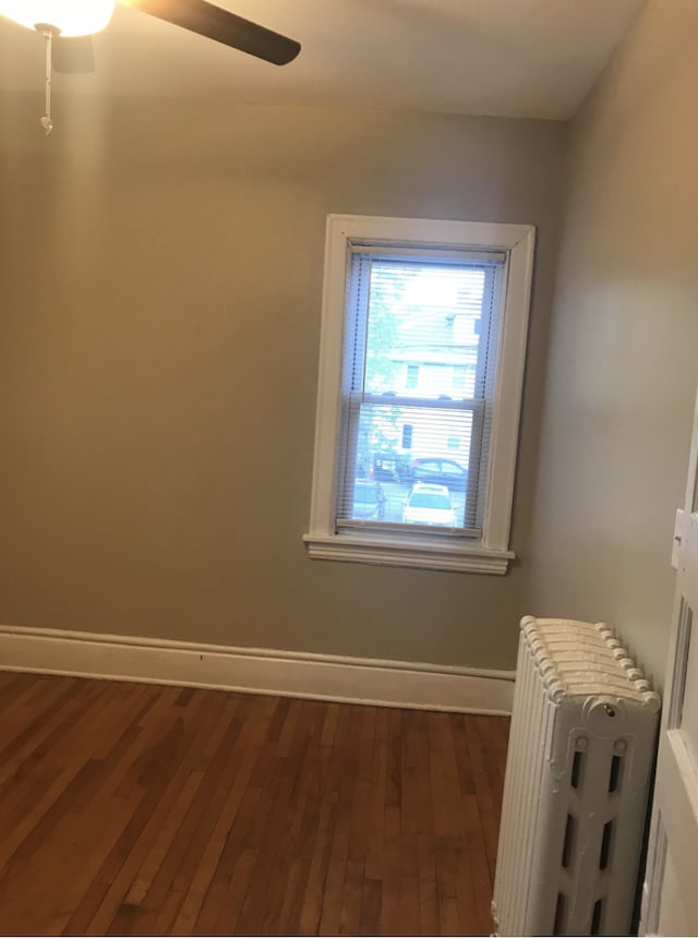 empty room featuring dark hardwood / wood-style flooring, ceiling fan, and radiator