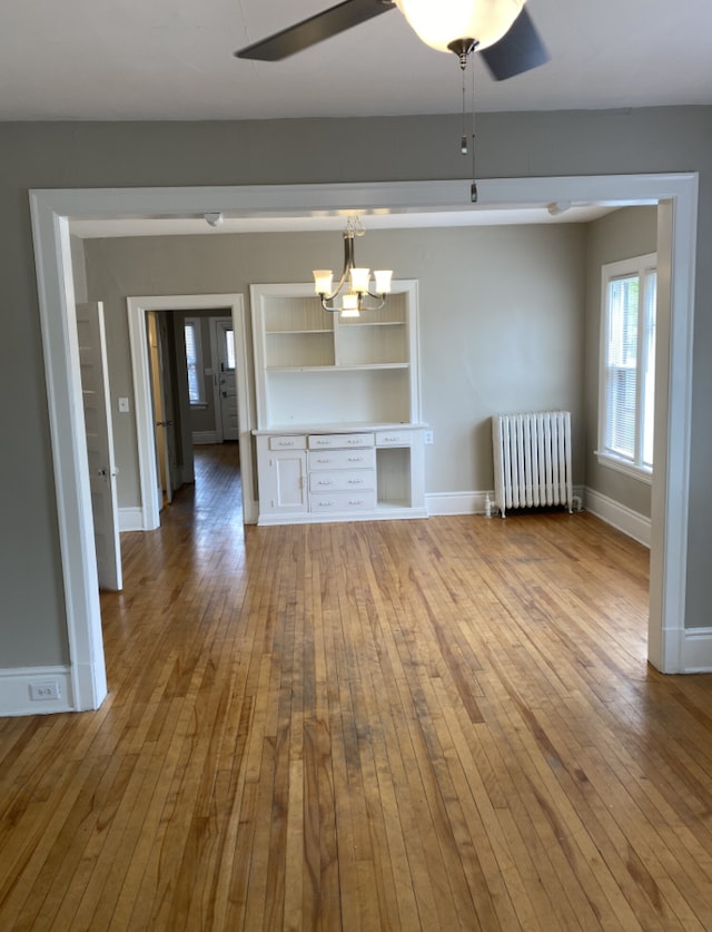 unfurnished living room featuring radiator heating unit, ceiling fan with notable chandelier, and hardwood / wood-style floors