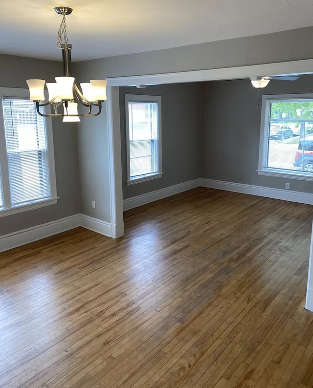 unfurnished room with a wealth of natural light, ceiling fan with notable chandelier, and hardwood / wood-style floors