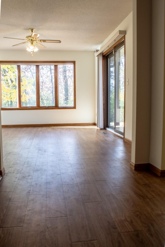 spare room with a textured ceiling, dark hardwood / wood-style floors, ceiling fan, and a healthy amount of sunlight