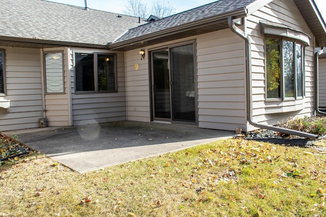 back of property with a yard, roof with shingles, and a patio area