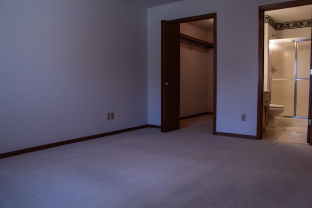 unfurnished bedroom with carpet flooring, a closet, a walk in closet, and ensuite bath