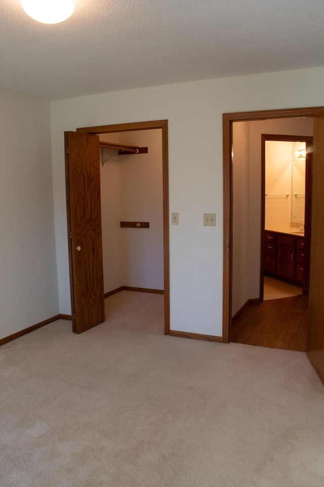 unfurnished bedroom with a textured ceiling, light colored carpet, a closet, and connected bathroom