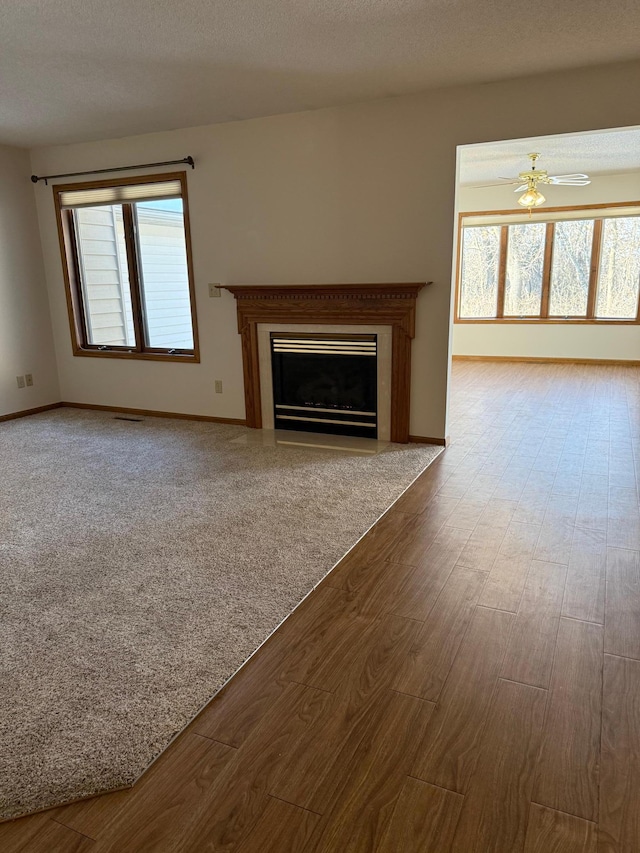 unfurnished living room featuring baseboards, visible vents, a fireplace with flush hearth, wood finished floors, and a textured ceiling