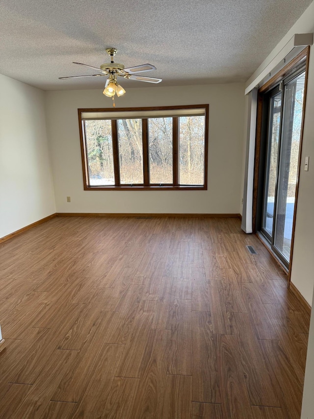 empty room with dark wood-style floors, a textured ceiling, visible vents, and baseboards