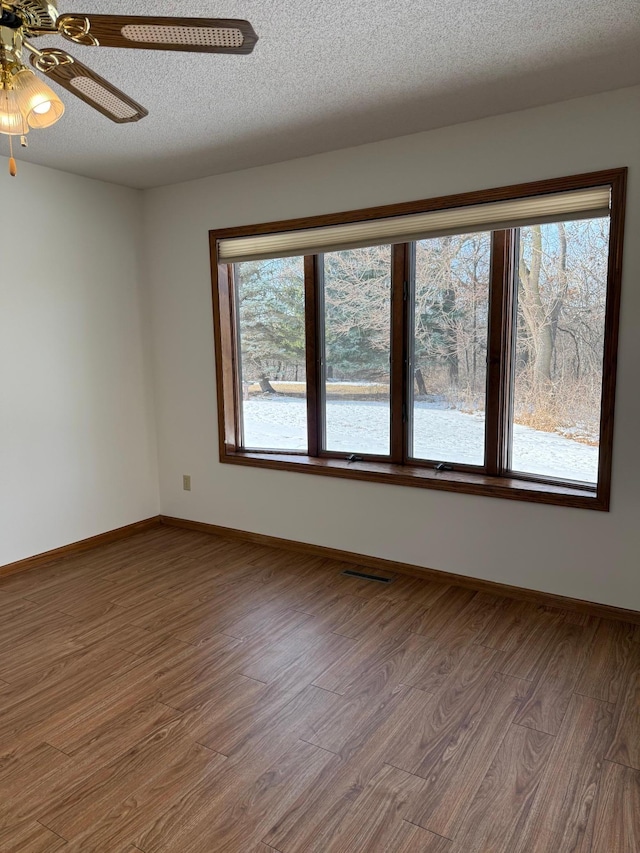 unfurnished room with a textured ceiling, wood finished floors, visible vents, and baseboards