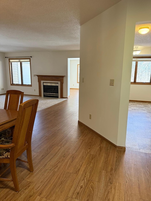 unfurnished dining area featuring a textured ceiling, wood finished floors, a glass covered fireplace, and a wealth of natural light