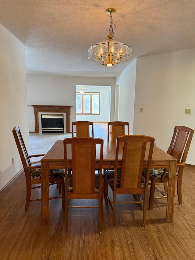 dining room with a textured ceiling, wood finished floors, baseboards, a glass covered fireplace, and an inviting chandelier