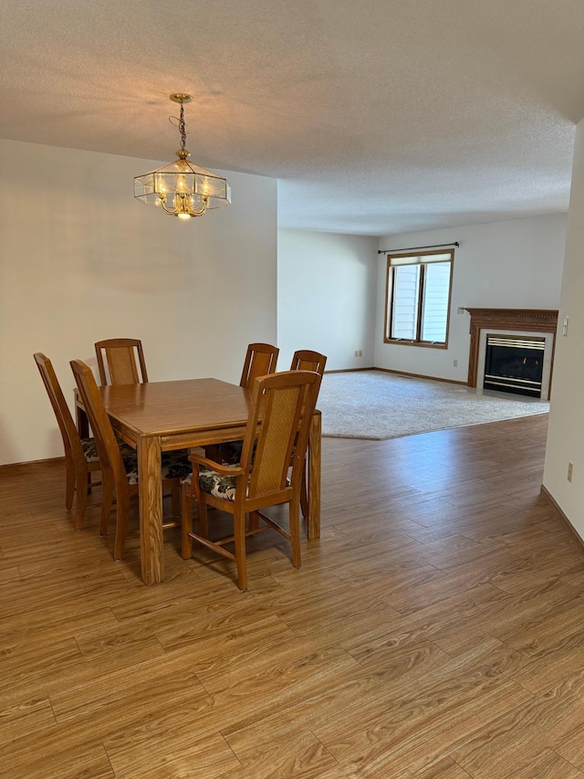 dining room featuring baseboards, a glass covered fireplace, a textured ceiling, light wood-style floors, and a chandelier