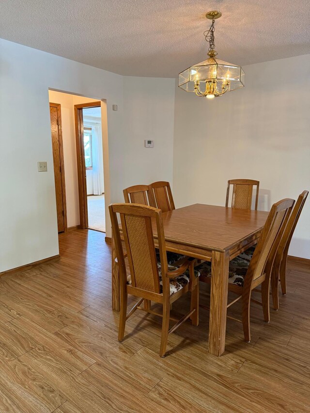 dining area with baseboards, a textured ceiling, light wood-style flooring, and an inviting chandelier