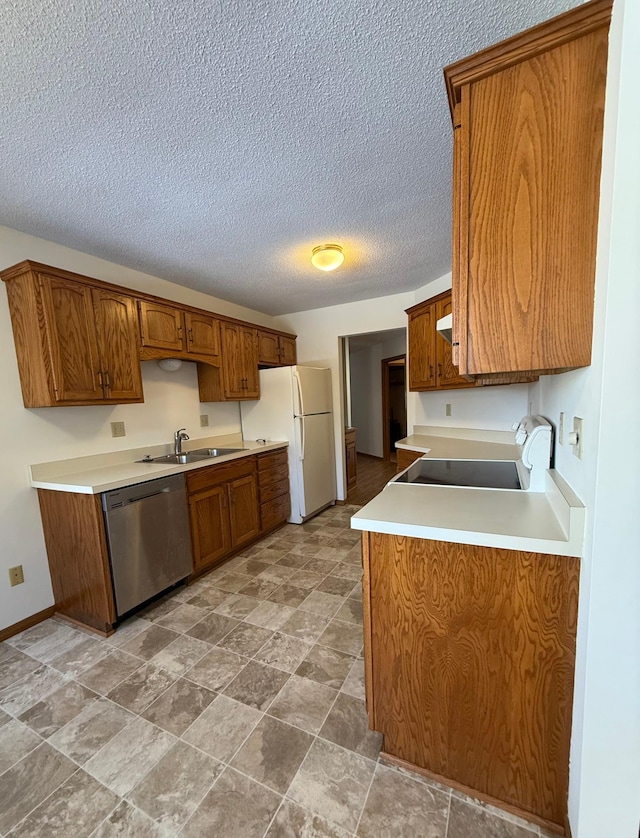 kitchen with brown cabinetry, freestanding refrigerator, a sink, and stainless steel dishwasher