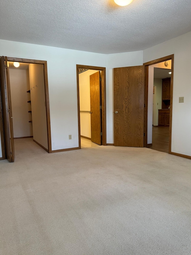 unfurnished bedroom featuring a closet, baseboards, a textured ceiling, and light colored carpet