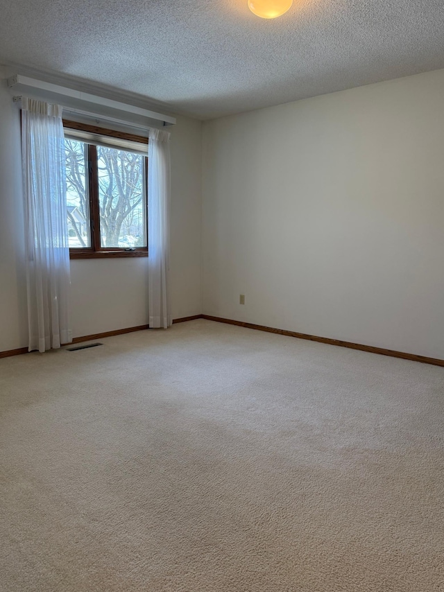 empty room featuring light carpet, baseboards, visible vents, and a textured ceiling