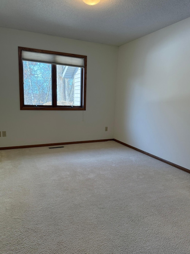 carpeted spare room with a textured ceiling and baseboards