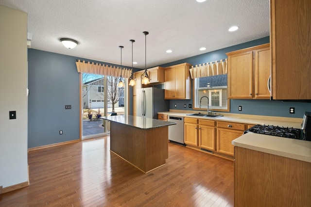 kitchen featuring stainless steel appliances, sink, wood-type flooring, pendant lighting, and a kitchen island