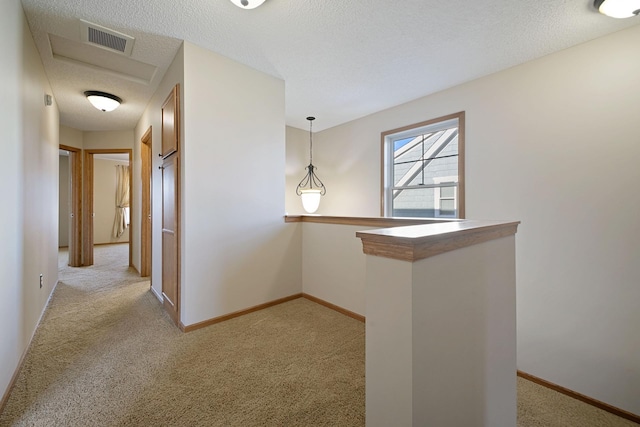 hallway with light colored carpet and a textured ceiling