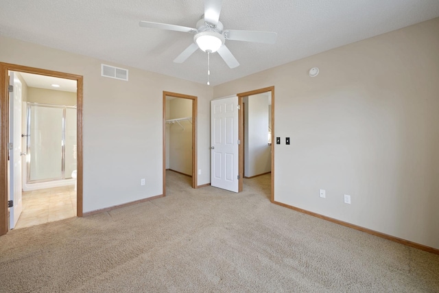 unfurnished bedroom with ensuite bathroom, ceiling fan, a spacious closet, light colored carpet, and a closet