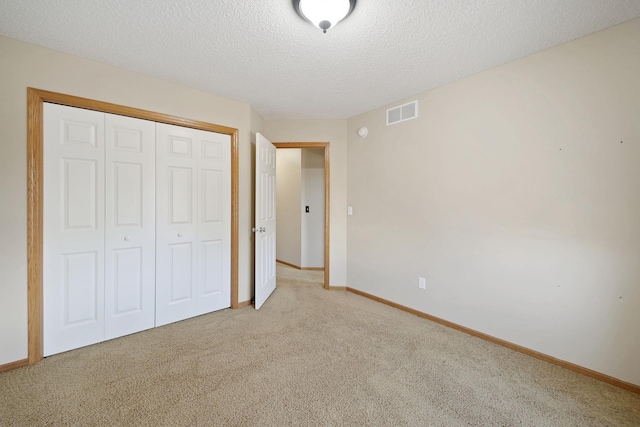 unfurnished bedroom featuring a textured ceiling, light carpet, and a closet