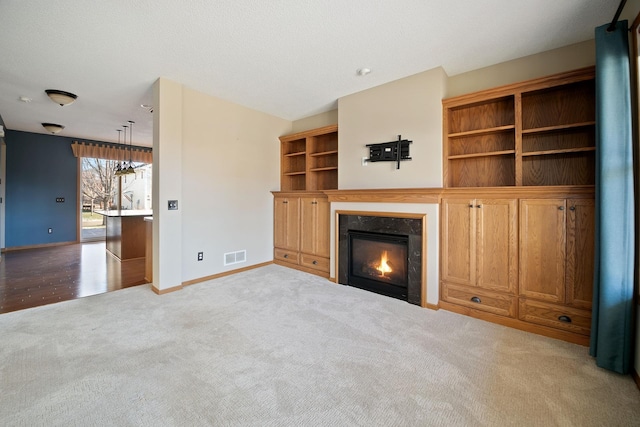 unfurnished living room featuring built in shelves, light colored carpet, and a textured ceiling