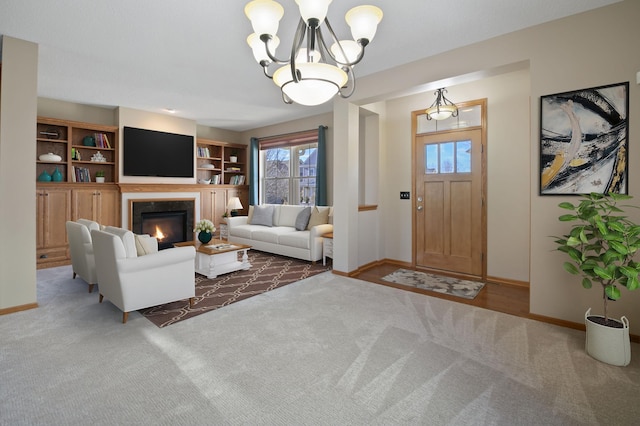 living room with a glass covered fireplace, an inviting chandelier, carpet flooring, and baseboards