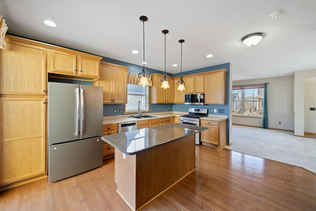 kitchen featuring stainless steel appliances, hanging light fixtures, light wood-style flooring, a sink, and a kitchen island