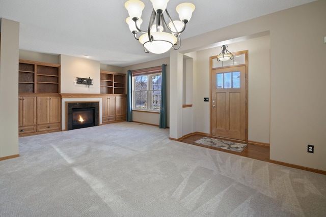 entryway with carpet floors, a glass covered fireplace, a notable chandelier, and baseboards