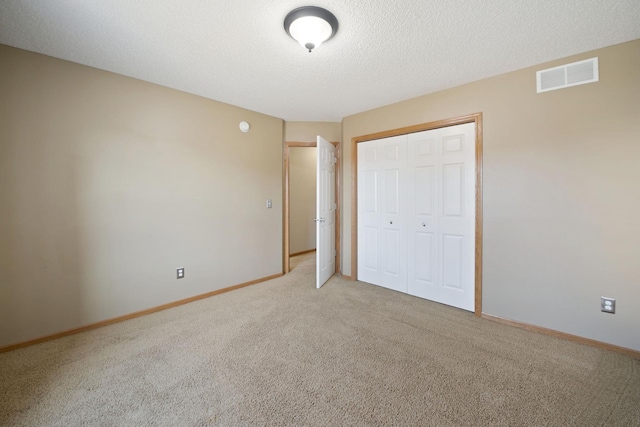 unfurnished bedroom featuring baseboards, visible vents, light colored carpet, a textured ceiling, and a closet