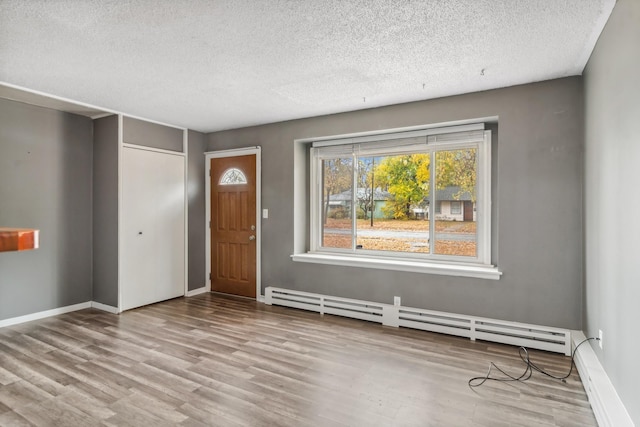 unfurnished room featuring a baseboard heating unit, a textured ceiling, and light wood-type flooring