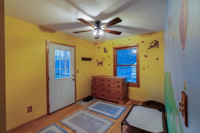 doorway featuring light hardwood / wood-style flooring, a textured ceiling, and ceiling fan