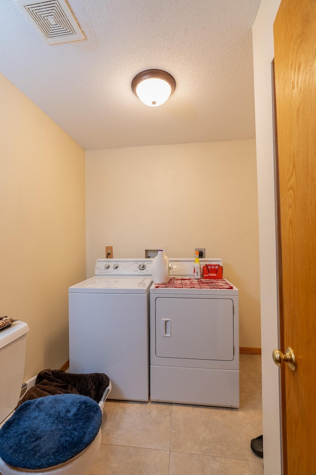 clothes washing area featuring a textured ceiling, independent washer and dryer, and light tile patterned flooring