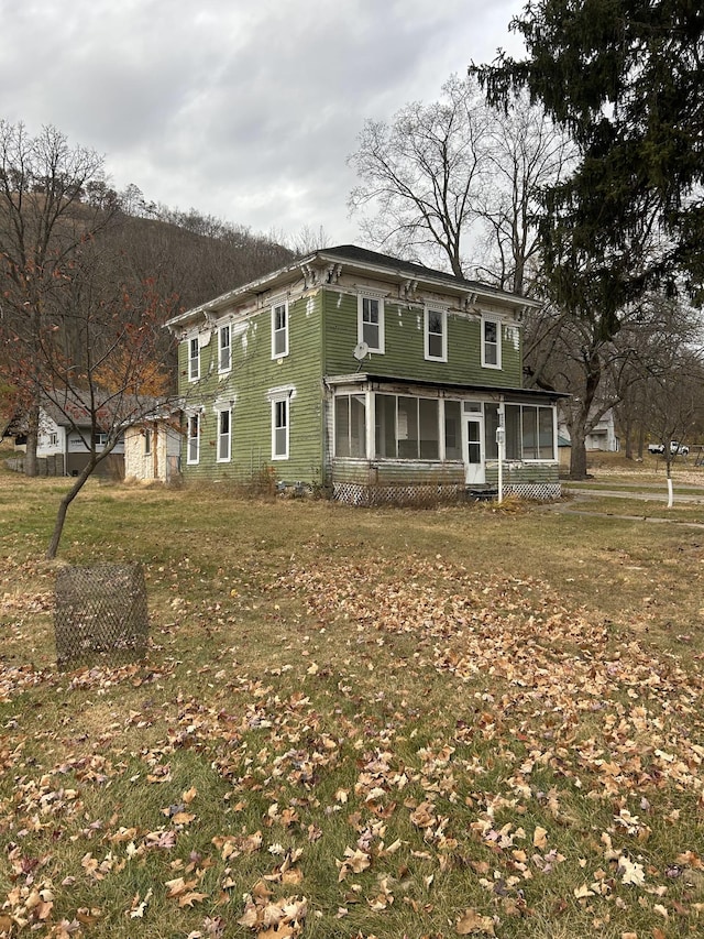 italianate-style house featuring a sunroom and a front lawn