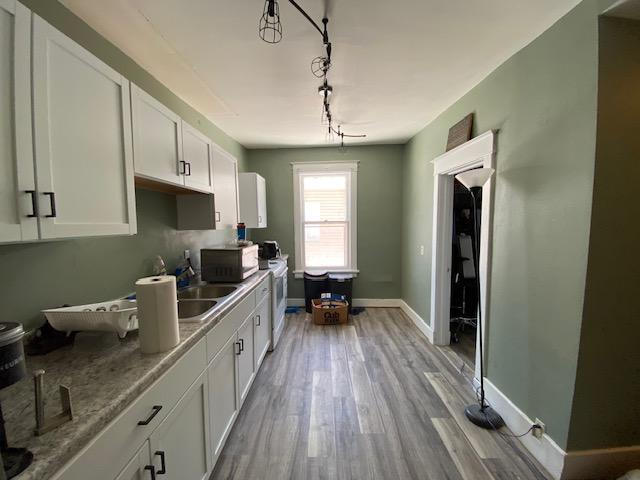 kitchen with light hardwood / wood-style flooring, sink, white cabinetry, light stone counters, and track lighting