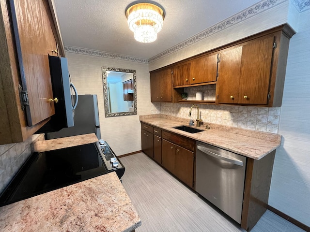 kitchen featuring sink, a chandelier, light stone counters, stainless steel appliances, and a textured ceiling