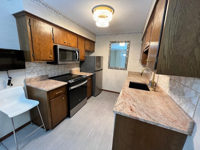 kitchen with sink, stainless steel appliances, light stone countertops, a textured ceiling, and an inviting chandelier