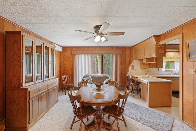 dining space featuring a wall unit AC, sink, ceiling fan, and wood walls