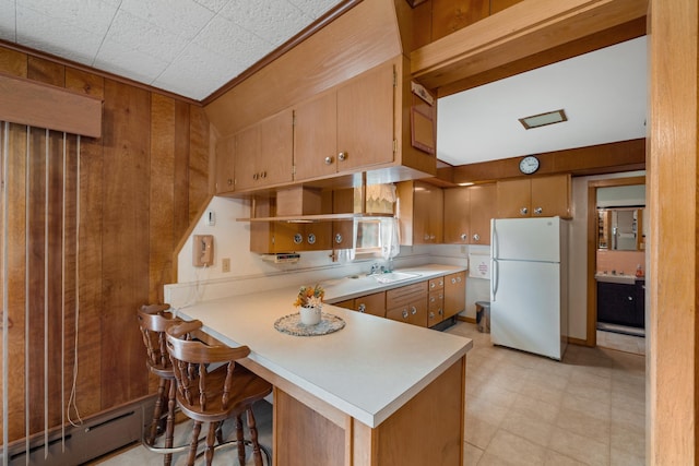 kitchen featuring kitchen peninsula, wood walls, baseboard heating, sink, and white refrigerator