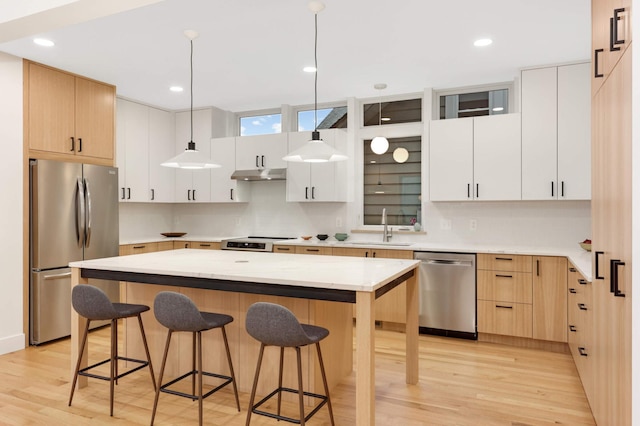 kitchen with white cabinets, light wood-type flooring, decorative light fixtures, a kitchen island, and stainless steel appliances