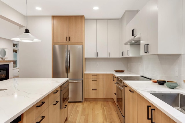 kitchen with white cabinetry, light stone counters, decorative light fixtures, appliances with stainless steel finishes, and light wood-type flooring