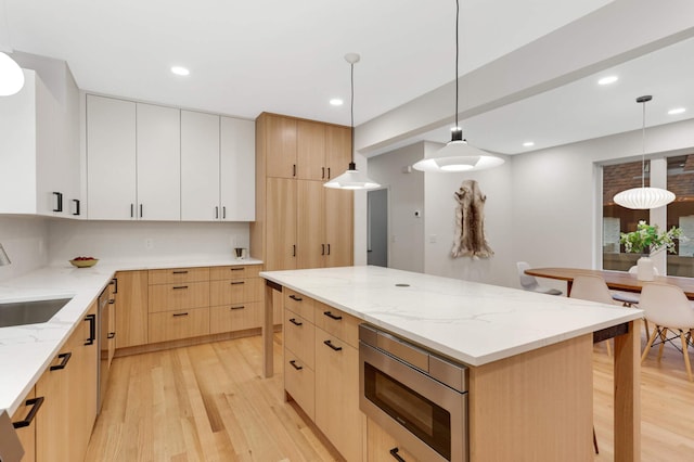 kitchen with stainless steel microwave, hanging light fixtures, light wood-type flooring, light stone counters, and white cabinetry