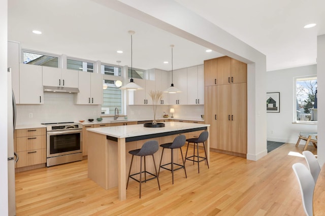 kitchen featuring pendant lighting, a center island, light wood-type flooring, stainless steel range oven, and white cabinetry