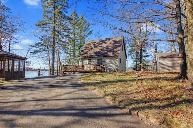 exterior space featuring driveway, a shingled roof, and a deck with water view