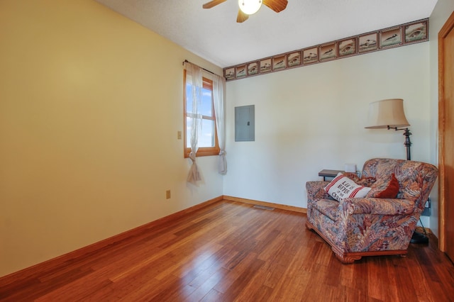 living area featuring electric panel, baseboards, wood finished floors, and ceiling fan