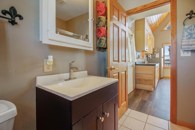 bathroom featuring vanity, visible vents, vaulted ceiling, tile patterned floors, and toilet