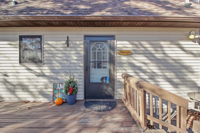 property entrance with a wooden deck and a shingled roof