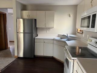 kitchen with white appliances, dark hardwood / wood-style flooring, sink, and white cabinets