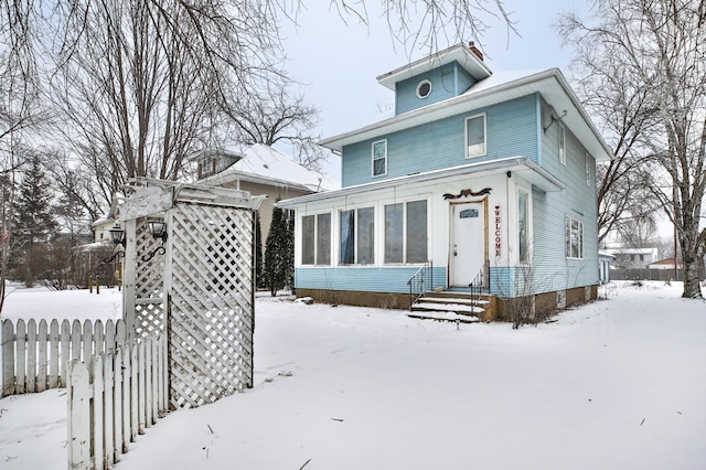 snow covered back of property with a sunroom